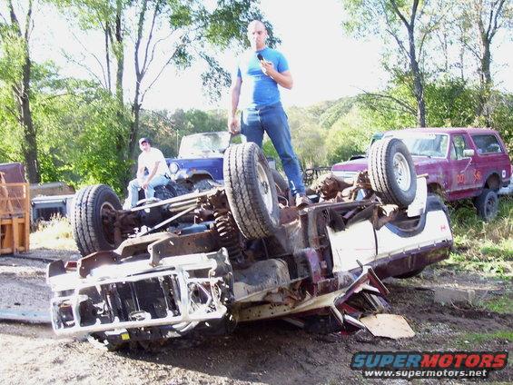guy standing on overturned vehicle chassis, another guy sitting on a blue jeep, purple bronco in background