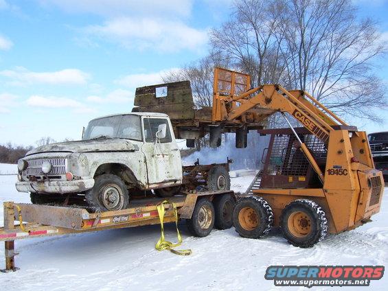 White pickup truck on trailer with skid steer loader, front 3/4 view
