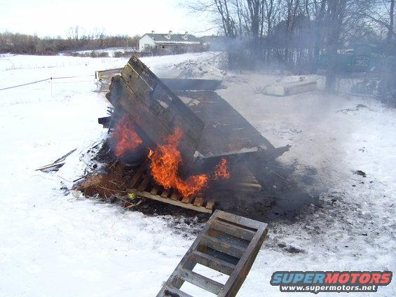Wooden structure on fire in a snowy field with a ladder in the foreground