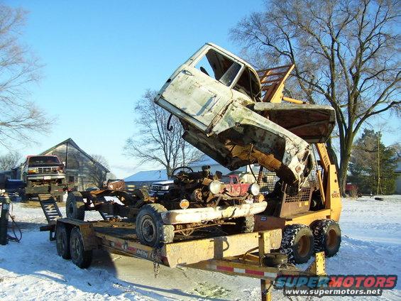 truck cab being lifted off chassis on trailer, another truck on flatbed in background