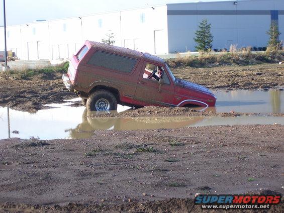 Red 1980s Ford Bronco stuck in mud puddle, 3q-front view