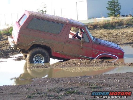 Red 1986 Ford Bronco stuck in a mud pit, front end submerged