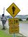 1972 Ford Ranchero - A man pauses near a "SLOW GEEZER CROSSING" sign, with a distant town visible.