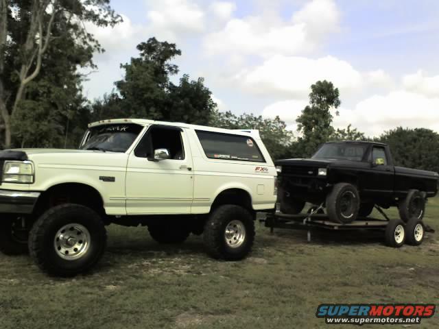 White SUV parked next to a black pickup truck being towed on a trailer