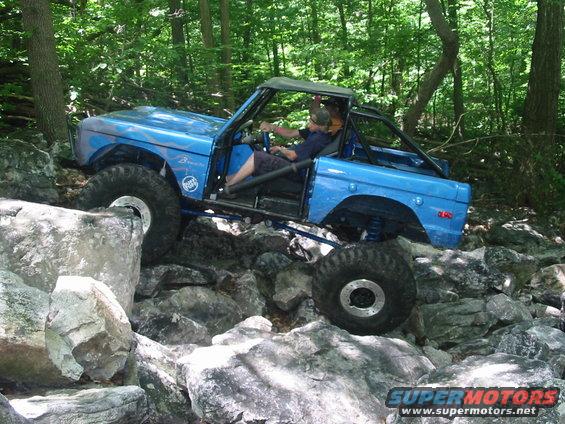 Blue off-road vehicle with large tires navigating a rocky trail in the woods