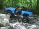 1969 Ford Bronco - This modified off-road vehicle is shown navigating a challenging rocky terrain in a wooded area.