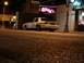 2003 Ford Crown Victoria - A white 2003 Ford Crown Victoria is parked on a city street at night, illuminated by streetlights and neon signs.