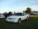 2003 Ford Crown Victoria - A white 2003 Ford Crown Victoria is parked on a grassy field with other vehicles in the background.