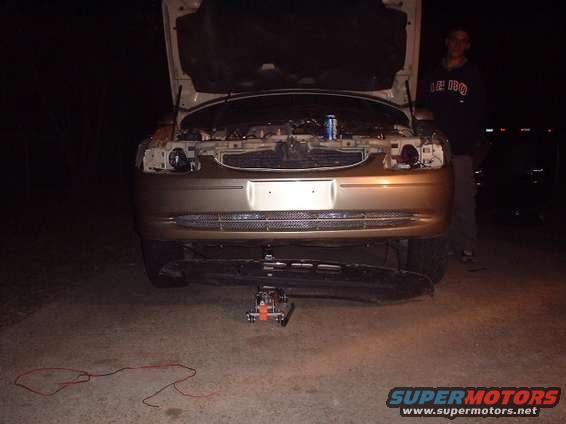 Gold sedan front end, hood open, jack under bumper