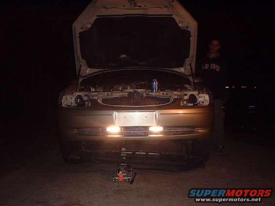 2000 Ford Taurus front end with hood open, showing engine bay and headlights illuminated