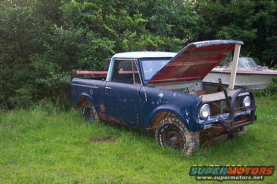 Blue pickup truck with hood open, parked in grass next to a boat