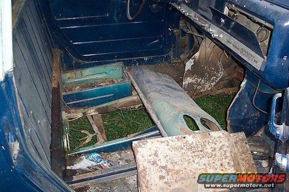 Dilapidated vehicle interior with rusted floor and torn seats. Text on dashboard reads 'INTERNATIONAL SCOUT 800'