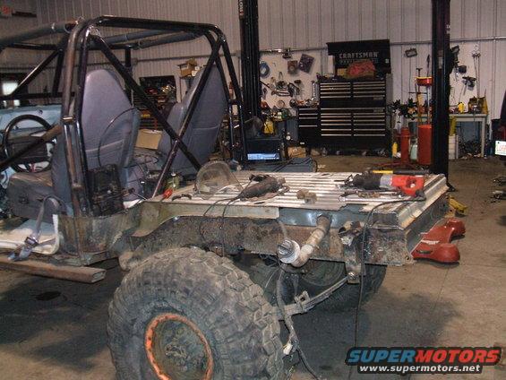 Back half of a Jeep CJ-7 with roll cage, seats, and exposed frame in a workshop