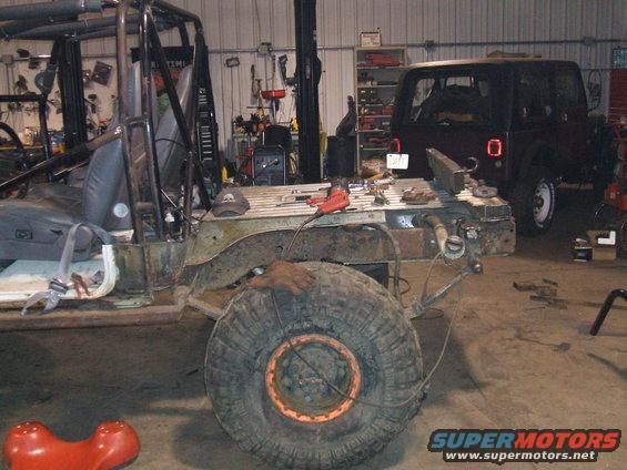 Off-road vehicle chassis with large tire, undergoing repairs in a workshop