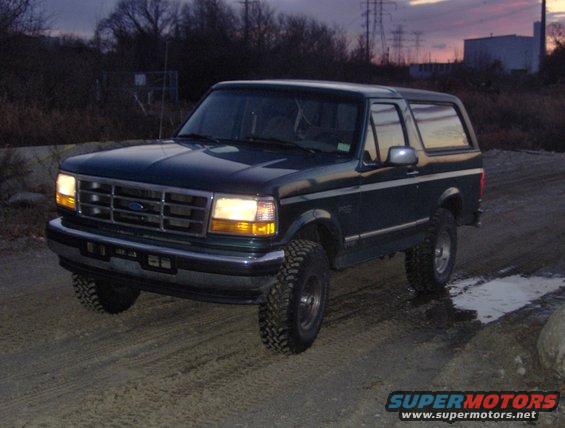 Dark green Ford Bronco with lifted suspension driving on a dirt road