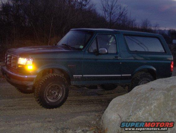 Green 1996 Ford Bronco parked on dirt with a large rock in the foreground