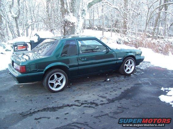 Green 1991 Ford Mustang coupe with 5.0 badging and aftermarket wheels in snow