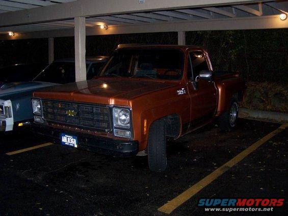 Orange 1979 Chevrolet C/K Pickup parked under a carport. Another vehicle is partially visible to the left