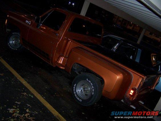 Orange pickup truck, rear quarter view, parked under a covered area