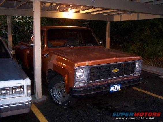 Orange 1979 Chevrolet C/K Pickup truck parked under a carport next to a white vehicle