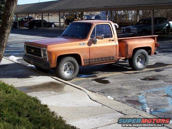 Orange 1979 Chevrolet C/K Pickup truck with black side graphics, parked on a slight incline