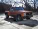 1979 Chevrolet C/K Pickup - A classic orange pickup truck is parked in a lot with bare trees in the background.