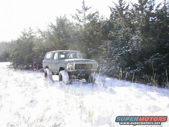 Green 1978 Ford Bronco with large tires driving in snow