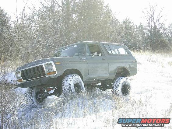 Olive green 1978 Ford Bronco with large tires driving in snow