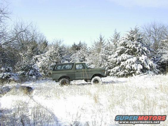 Green 1978 Ford Bronco parked in a snowy field with snow-covered trees