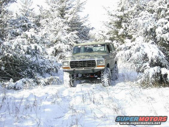 1978 Ford Bronco driving on a snowy trail with trees covered in snow