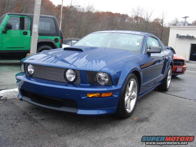 Blue Ford Mustang parked outside a building, with a green Jeep and an orange car behind it