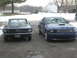 2007 Ford Mustang - Two Ford Mustangs, a modern blue one and a classic dark one, parked outside in winter.