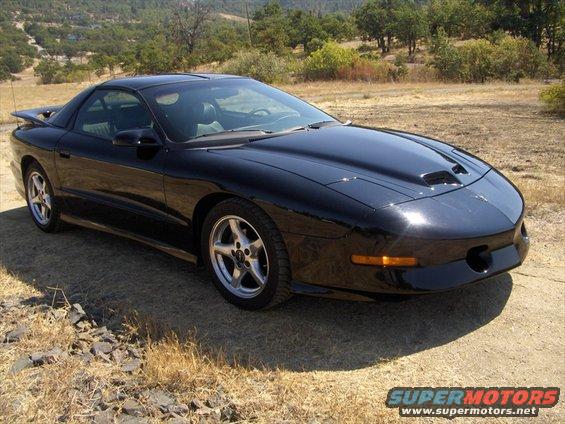 Black 1997 Pontiac Firebird parked on a dirt road with trees and hills in the background