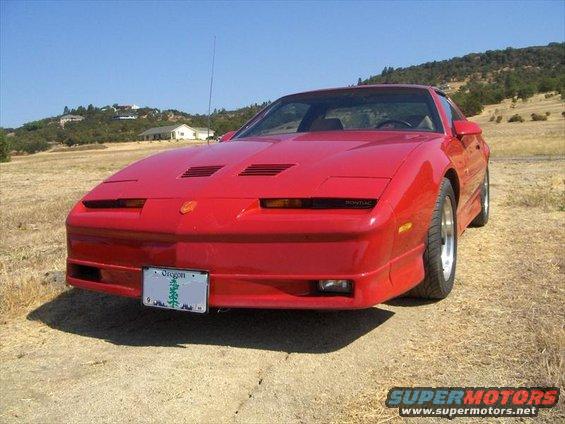 Red Pontiac Firebird parked on a dirt road with hills in the background