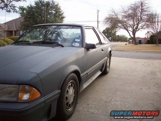 Gray Ford Mustang coupe with a matte finish, parked on a concrete driveway. Visible side trim reads 'Mustang'