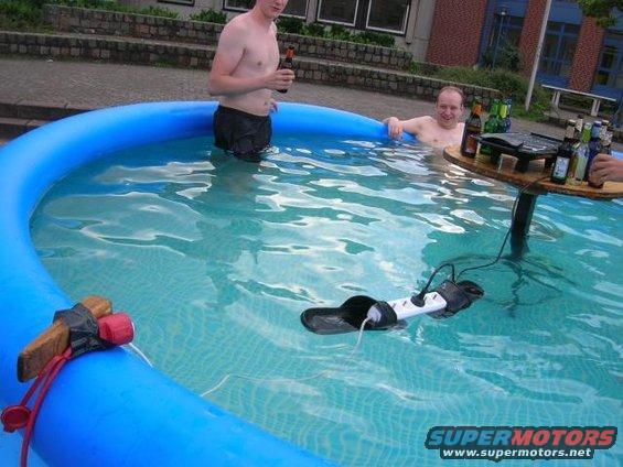 Inflatable pool scene with two men, beer, and a floating power strip