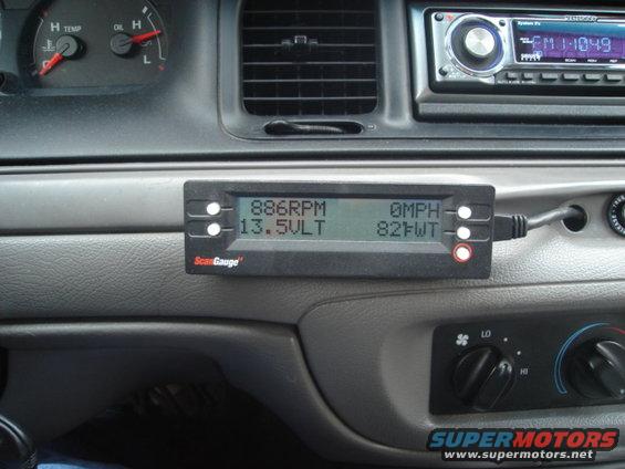 Dashboard of a 2000 Ford Crown Victoria showing a ScanGauge II displaying RPM, voltage, speed, and temperature