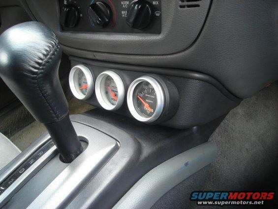 Car interior showing gear shifter and three aftermarket gauges mounted on the center console