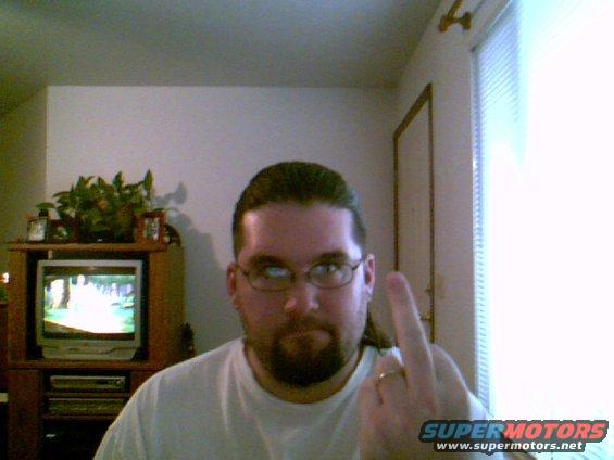guy with glasses and ponytail flipping the bird, TV in background
