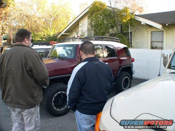Two men stand by a maroon 2007 Toyota FJ Cruiser. Another vehicle is partially visible on the right
