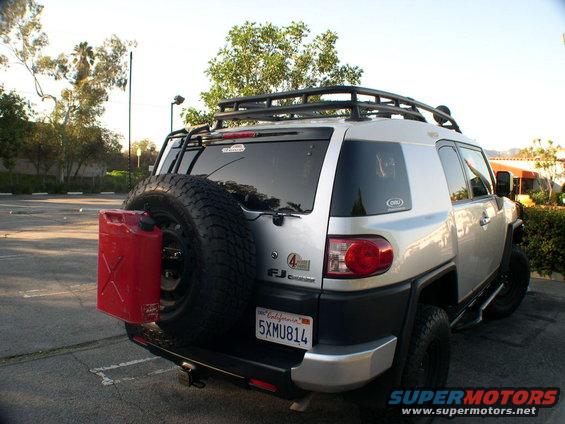 Rear view of a silver 2007 Toyota FJ Cruiser with a spare tire and red gas can mounted on the back. It has a roof rack and a California license plate