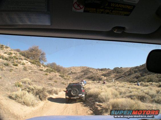Black 2007 Toyota FJ Cruiser driving on a dirt road in a dry, hilly landscape