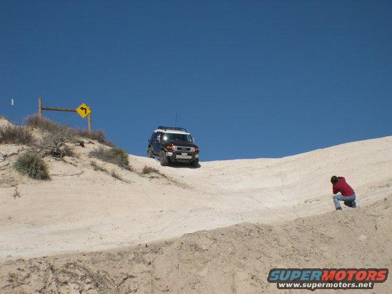 2007 Toyota FJ Cruiser driving up a sandy incline with a person photographing it