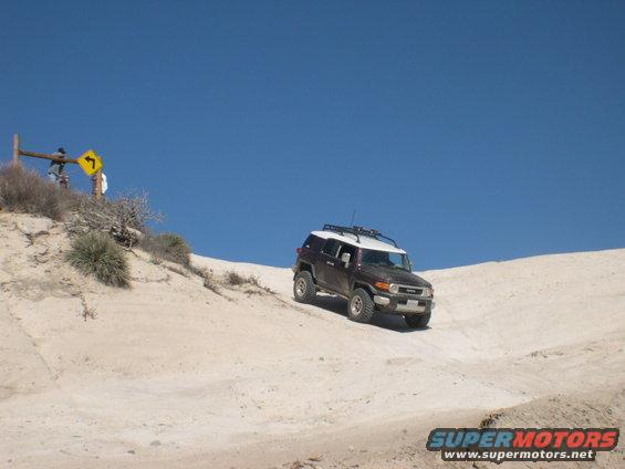 Dark brown 2007 Toyota FJ Cruiser with a white roof and roof rack driving on a sandy hill