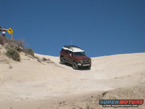 Red and white 2007 Toyota FJ Cruiser driving down a sandy slope