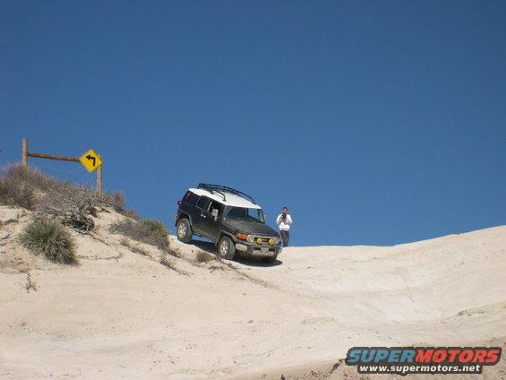 2007 Toyota FJ Cruiser driving on a sandy hill with a person standing nearby