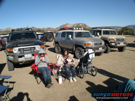 Three Toyota FJ Cruisers parked in a desert; two people sit in chairs in foreground
