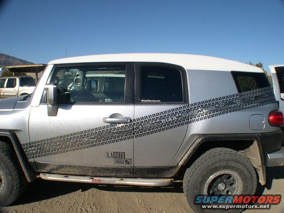 Side view of silver 2007 Toyota FJ Cruiser with tire track decals and 'LA Auto Show' sticker