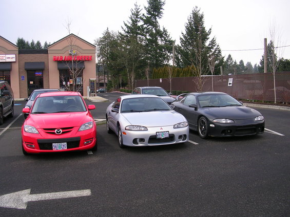Red 2007 Mazda 3 front view, parked next to two Mitsubishi Eclipses