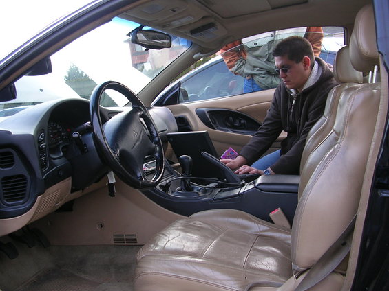 Interior view of a car, showing the dashboard, steering wheel, and a person using a laptop on the center console